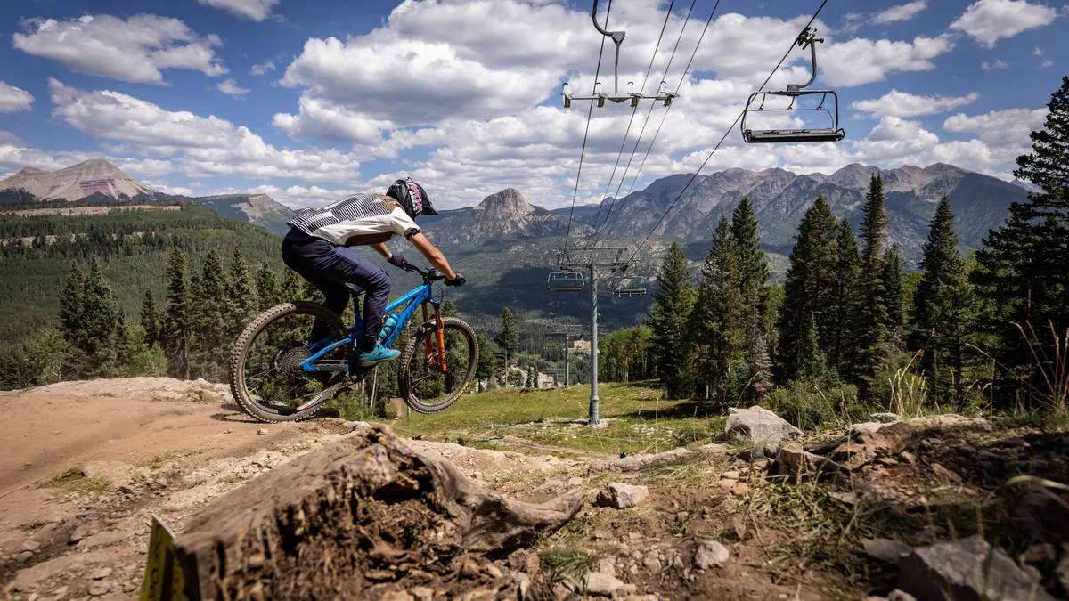 A dynamic exterior scene featuring a mountain biker riding through the rugged landscape, with ski lifts and towering mountains in the background. The setting radiates excitement and possibility, perfect for families who cherish active vacations, hiking, and exploring the outdoors together.