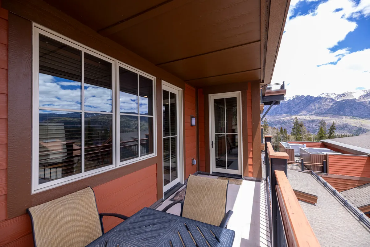 This image presents a private balcony seating area overlooking breathtaking mountain vistas, framed by large windows. The tranquil setting is perfect for sipping coffee at sunrise, relaxing with a book, or enjoying sunset drinks while soaking in sweeping alpine views.