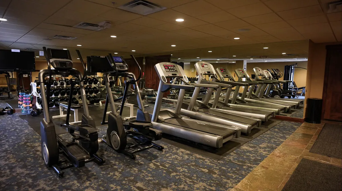 A modern, well-equipped fitness center featuring treadmills, ellipticals, dumbbells, and a mirrored wall. The space is bright and motivational, hinting at group classes or personal workouts. The gym is immaculate and welcoming, underscoring wellness as a core amenity.