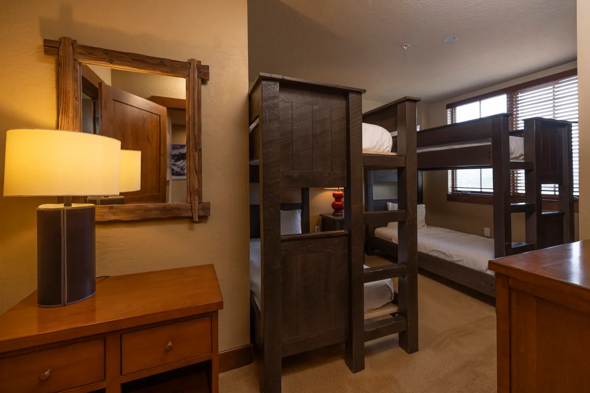 This playful bunk room features bunk beds, a wooden dresser, a lamp, and a mirror. The space is designed for kids or groups, fostering fun and cozy moments before bedtime.