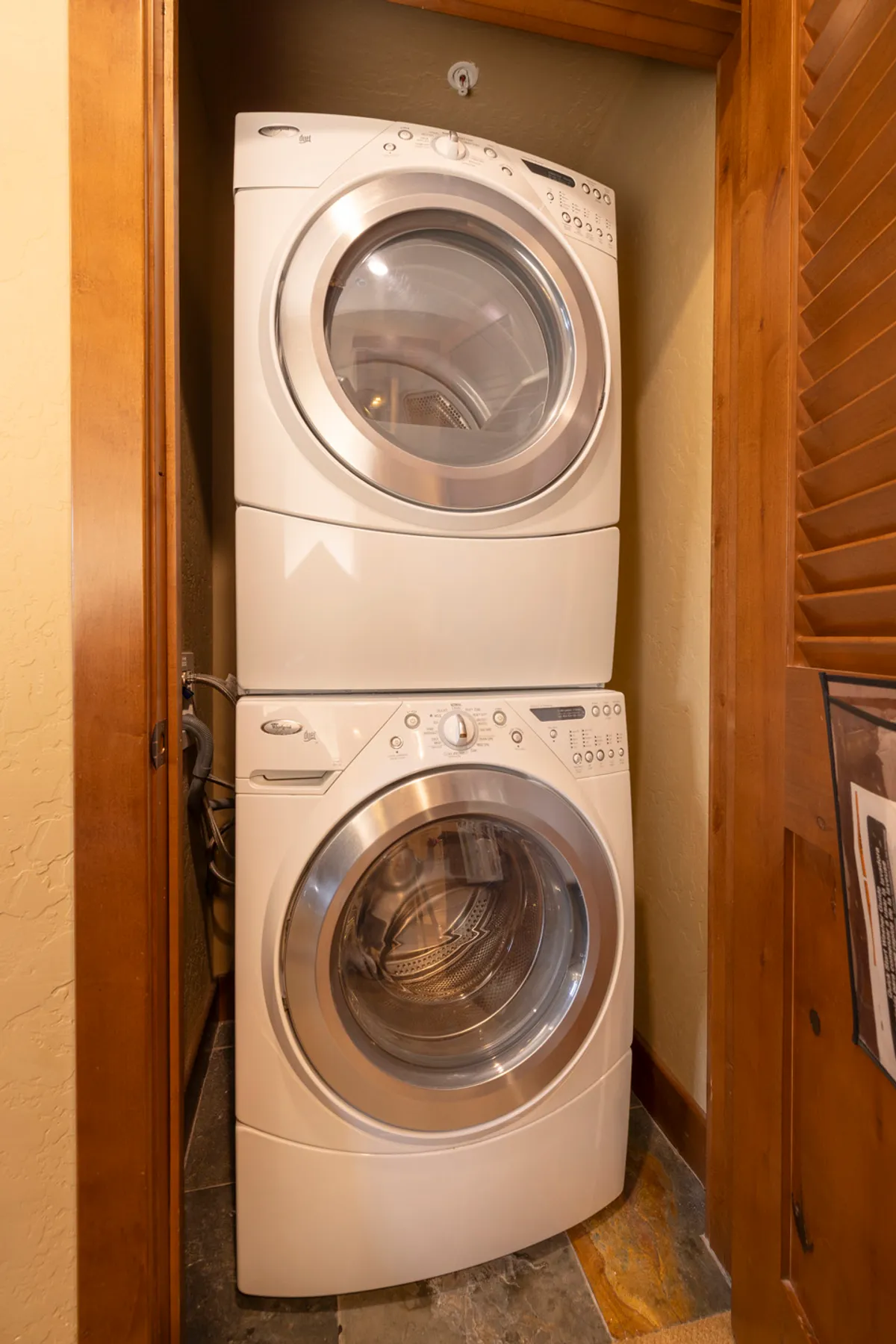 A compact, efficient laundry area with stacked washer and dryer, wooden cabinetry, and slate flooring. An often-overlooked interior amenity, it highlights practical aspects of the basecamp experience, including easy gear care after a day outdoors.