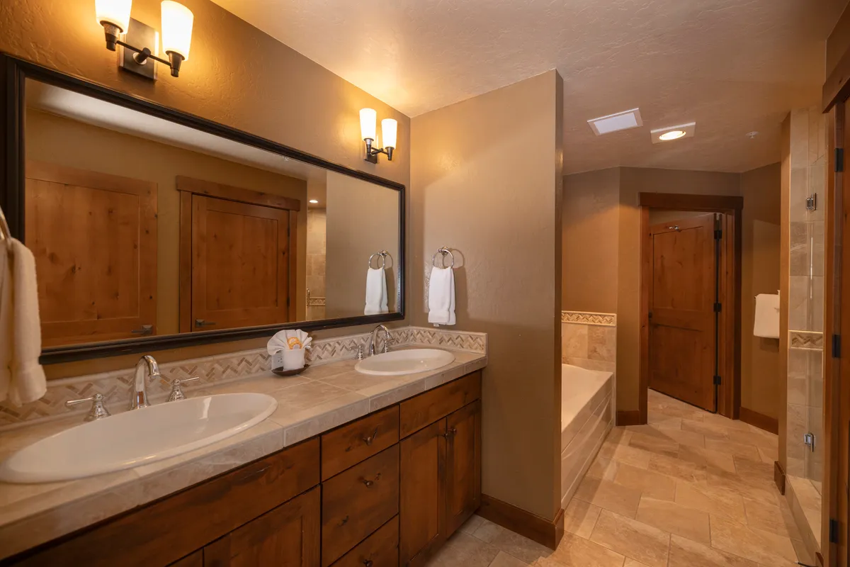 A bright, tranquil bathroom with double vanity sinks, a large mirror, warm wood cabinetry, and a bathtub. The environment is serene, designed for relaxation and rejuvenation.